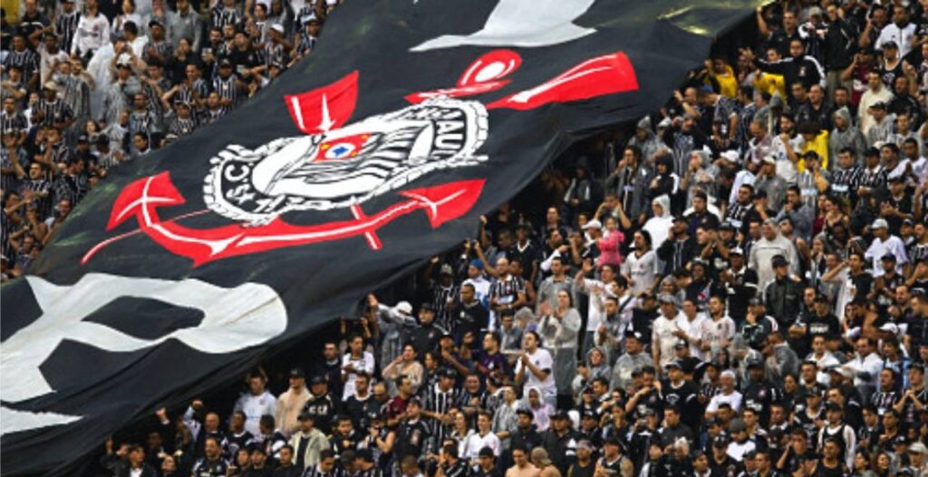 Bandeirão do Corinthians com escudo do clube e torcida lotando arquibancada do estádio