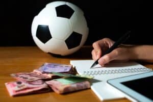 bola de futebol, caderno e dinheiro em cima de uma mesa, com apostador fazendo anotações