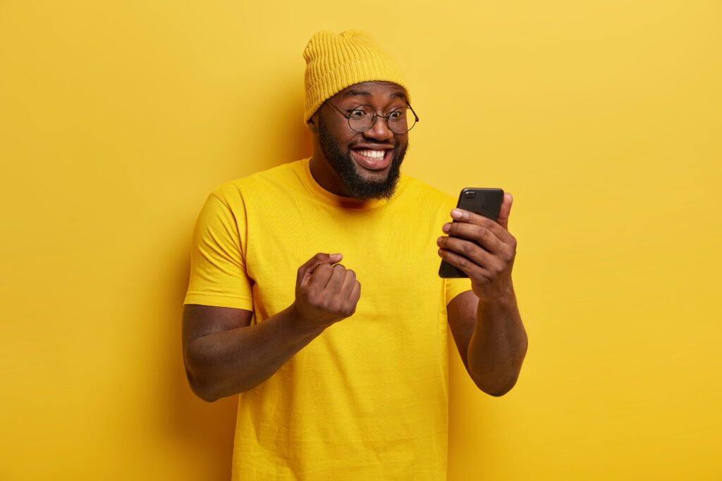 Homem negro mexendo no celular e vibrando por uma vitória