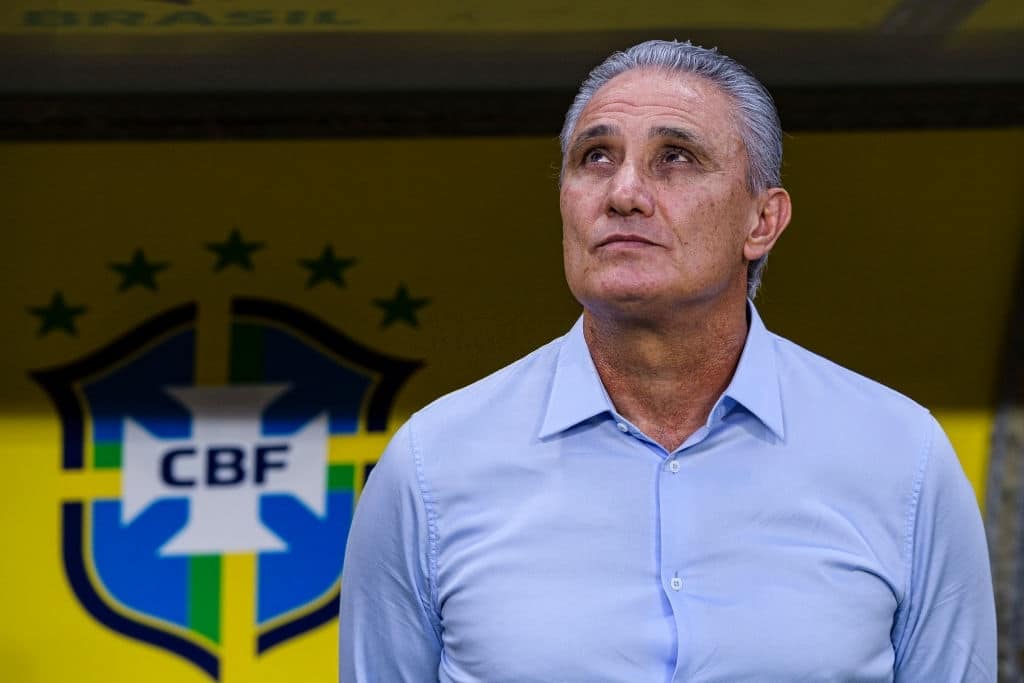 Tite, técnico da Seleção Brasileira, olhando para cima e, de fundo, o escudo da CBF