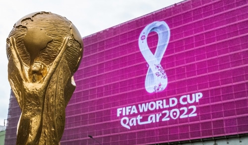 Taça da Copa do Mundo em primeiro plano; Logo da Fifa World Cup Qatar 2022 ao fundo