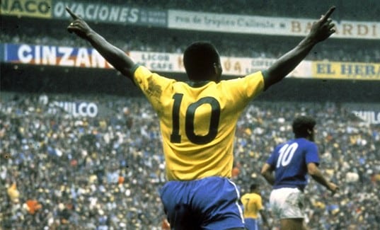 De costas, Pelé vestindo a camisa amarela da Seleção Brasileira, com o número 10, com braços erguidos, no gramado, diante de estádio lotado