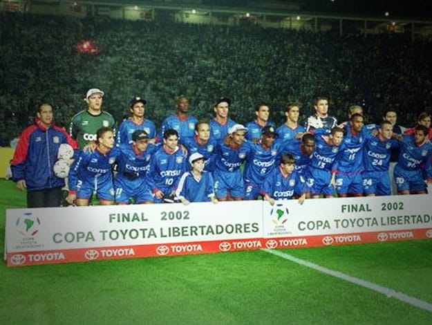 Time do São Caetano de 2002, perfilada atrás da placa da final da Libertadores de 2002.