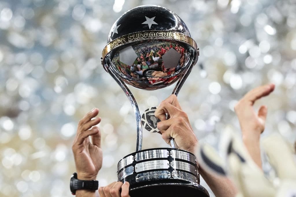 Taça da Copa Sul-Americana, em close, sendo erguida por mãos de homem