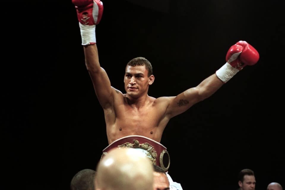 Lutador de boxe Popó após vencer uma luta, de braços erguidos, no ringue, com luvas e o cinturão de campeão
