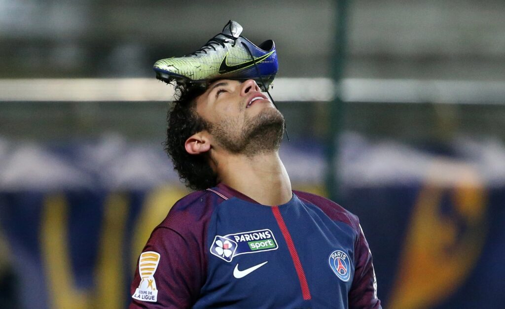 Neymar vestindo camisa do PSG e equilibrando chuteira na testa, como se fosse uma bola.