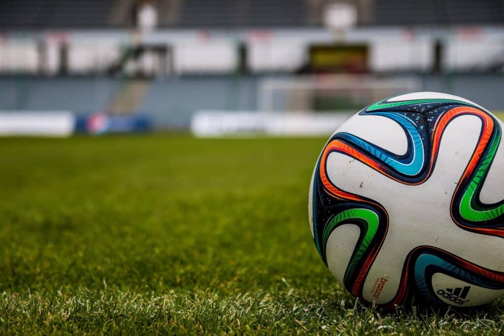 Bola de futebol posicionada na lateral direita da imagem. Ao fundo, arquibancadas de um estádio
